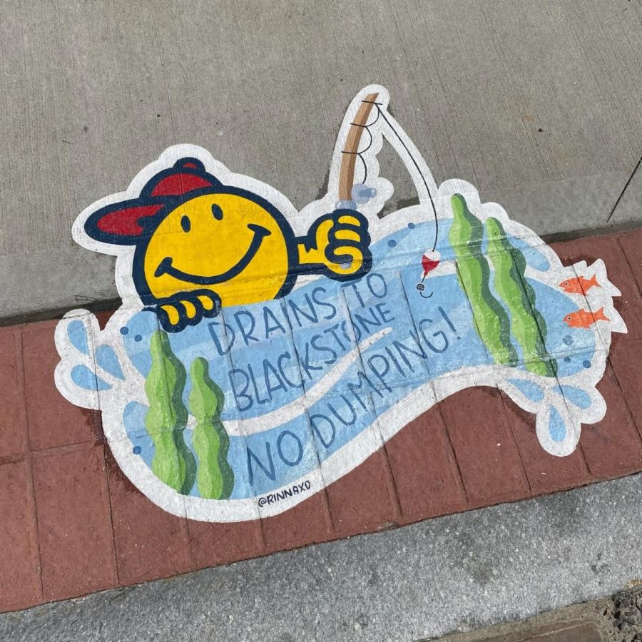 Sidewalk mural of a yellow smiley face character fishing in a stream, with the message “Drains to Blackstone – No Dumping!” surrounded by green plants and small orange fish. Sponsored by the Worcester Red Sox.