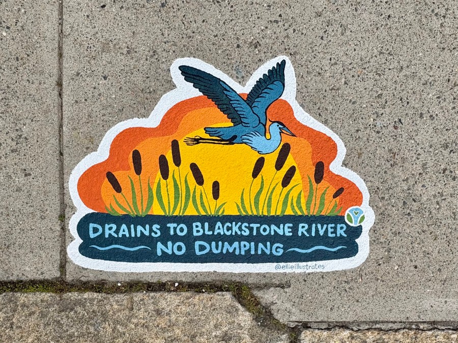 Close-up of a colorful sidewalk mural featuring a blue heron in flight above cattails with a warm orange sky behind it. The text at the bottom reads “Drains to Blackstone River – No Dumping.”