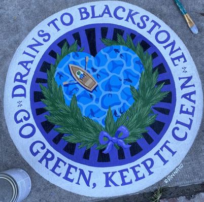 Circular catch basin mural with a heart-shaped river scene and a boat, framed by green leaves and purple ribbon. Text reads “Drains to Blackstone – Go Green, Keep It Clean.” Sponsored by Major Bloom.